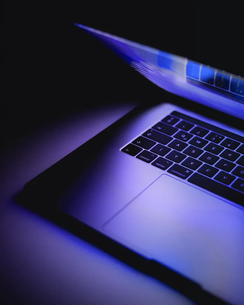 Un ordinateur portable entrouvert, son écran diffuse une lumière bleue et violette