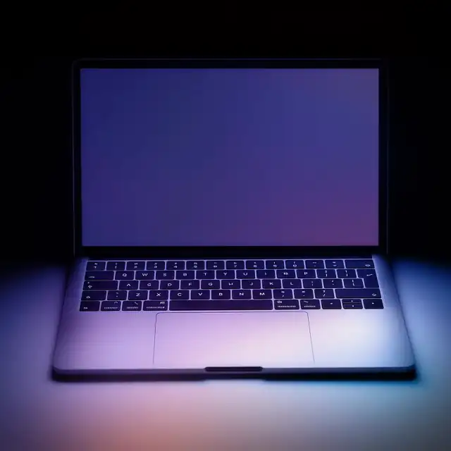An open laptop in the dark, its screen lighting the keyboard