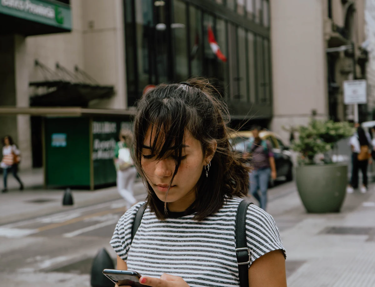 Une jeune femme cherche une adresse sur son téléphone, dans la rue